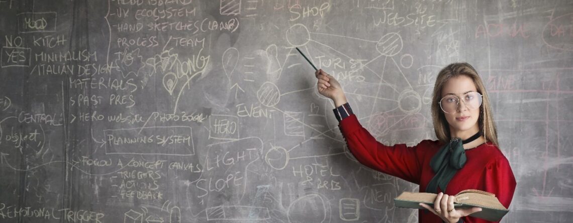 Teacher holding a book and point at a blackboard.