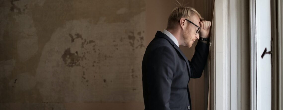 A man in a black suit standing near a window