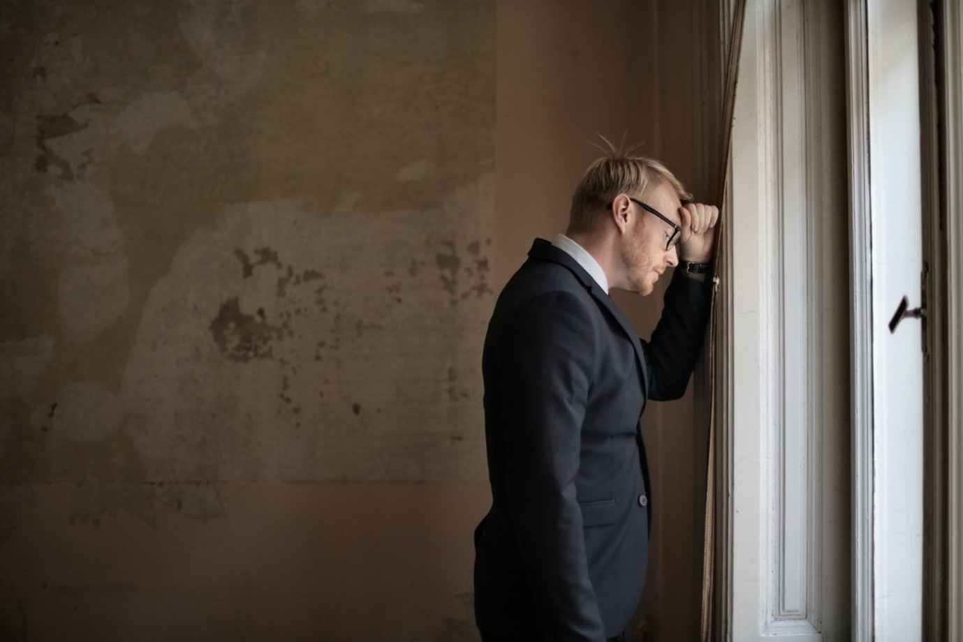 A man in a black suit standing near a window